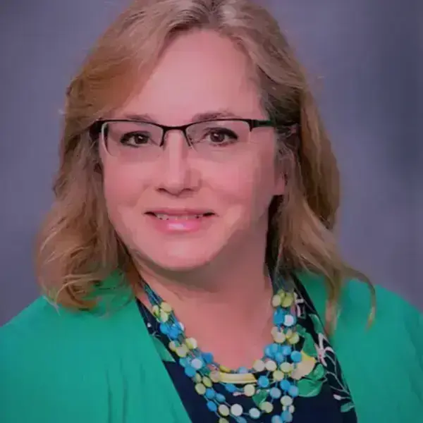 Woman with blonde hair wearing glasses and a green cardigan smiles.